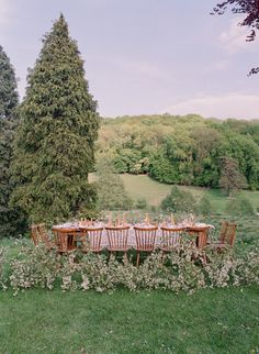 an outdoor dining table set up in the middle of a field with trees and flowers