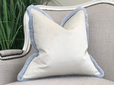 a white and blue pillow sitting on top of a couch next to a green plant