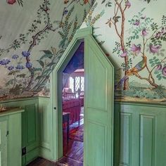 an open door in the corner of a room with floral wallpaper and green cupboards