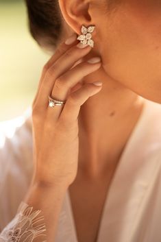 a woman wearing a ring with flowers on it's middle finger and holding her hand up to her ear