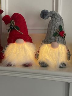 two gnomes sitting on top of a mantle with christmas lights in their ears and tails