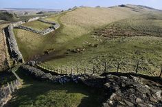 an aerial view of a stone wall in the middle of a grassy field with hills and fields behind it