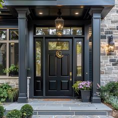 a black front door with two potted plants on the steps and lights above it