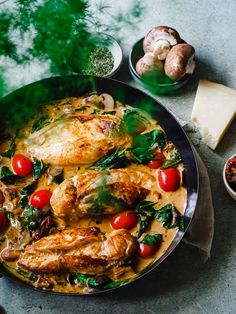 a pan filled with chicken, tomatoes and spinach on top of a table next to cheese