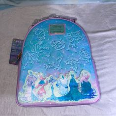 a blue and purple backpack with princesses on it sitting on a white sheet covered bed