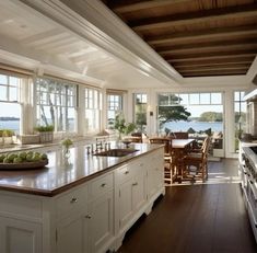 a large kitchen with an island counter top and wooden flooring, along with windows overlooking the water