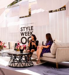 two women sitting on couches talking in front of a sign that says style week 00