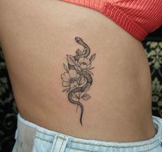 a woman's stomach with a snake and flowers tattoo on her side ribcage