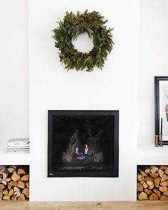 a fireplace with a wreath on the wall and firewood stacked in front of it