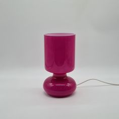 a pink glass sitting on top of a table next to a white wall behind it