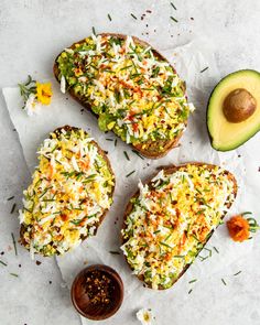 three toasted breads topped with shredded cheese and vegetables next to an avocado