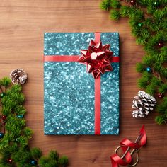 a present wrapped in blue paper with a red ribbon and bow on it next to christmas decorations