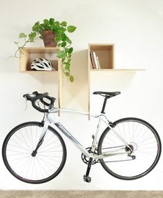 a bicycle is parked in front of a wall mounted shelf with books and a potted plant