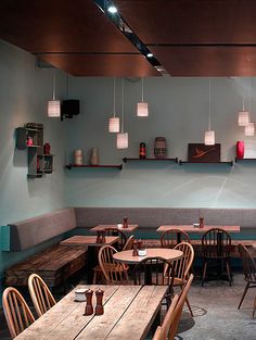 an empty restaurant with wooden tables and chairs in front of a wall filled with hanging lights