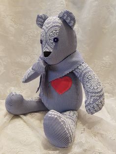 a blue and white teddy bear with a red heart on it's chest sitting on a bed