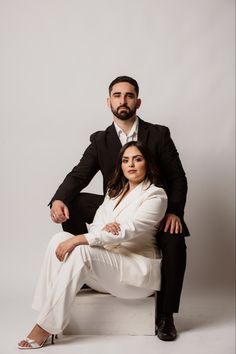 a man and woman posing for a photo in formal wear, sitting on a stool