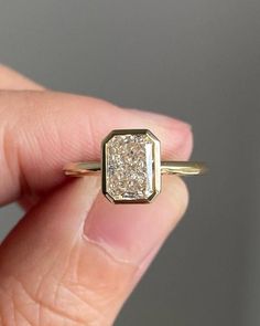 a hand holding a gold ring with a square diamond in it's center and the middle