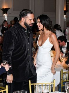 a man and woman standing next to each other at a table with wine glasses on it