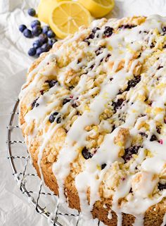 a lemon blueberry cake with icing on a wire rack next to some fruit