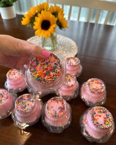 a hand is picking up some pink frosted cupcakes with sprinkles