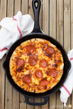 a pepperoni pizza in a cast iron skillet on a wooden table with napkins