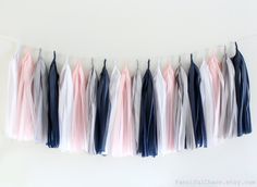 some tassels are hanging from a string on a white wall with blue, pink and grey colors