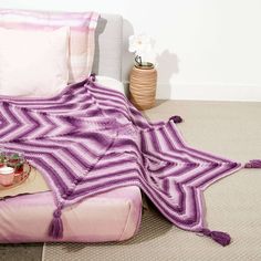 a purple blanket sitting on top of a bed next to pillows and a potted plant