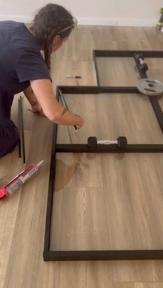 a woman laying on the floor with tools in front of her and working on an unfinished piece of furniture