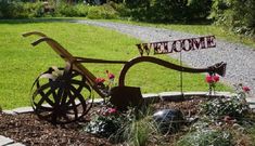 a welcome sign in the middle of a flower bed with flowers and a wheel on it