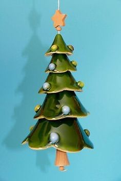 a green ceramic christmas tree ornament hanging from a string on a blue wall