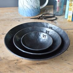 three black bowls sitting on top of a wooden table next to a cup and scissors