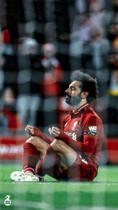 a soccer player sitting on the ground with his foot up in front of him and looking at something