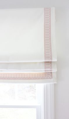 a window with a white and pink roman blind on it's side, in front of a window sill