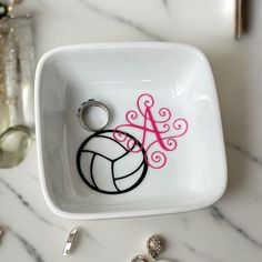 a white bowl with a pink monogrammed volleyball keychain on it next to other accessories