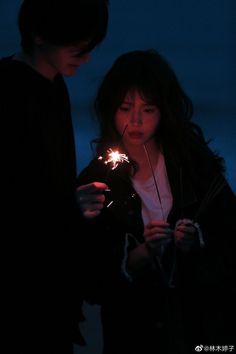 two people standing next to each other holding sparklers in their hands and looking at them