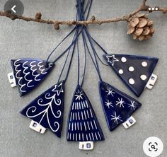 blue ceramic ornaments hanging from a branch with pine cones in the background and snowflakes on them