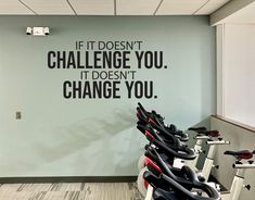 there are many exercise bikes lined up in the gym with words on the wall behind them