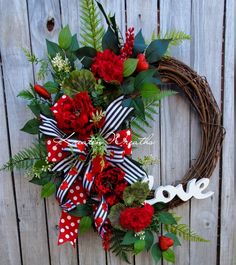 a wreath with red flowers and greenery is hanging on a wooden fence next to a love sign