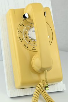 an old fashioned yellow telephone sitting on top of a white table next to a wall