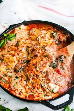 a skillet filled with cheese and sauce on top of a white table cloth next to green leaves