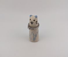 a white and blue cat figurine sitting on top of a bottle with a chain around it's neck