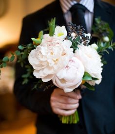 a man in a tuxedo holding a bouquet of white peonies and greenery