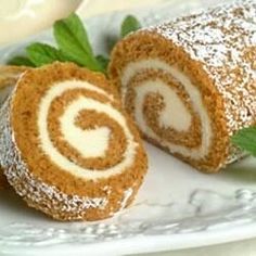 a roll is on a plate with powdered sugar sprinkled around it and green leaves