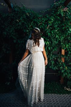 a woman wearing a white dress standing in front of green plants