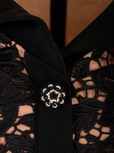 the collar of a black lace shirt with a brooch on it's lapel