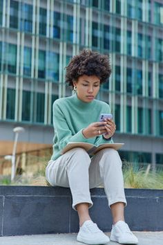 a woman sitting on a ledge looking at her cell phone