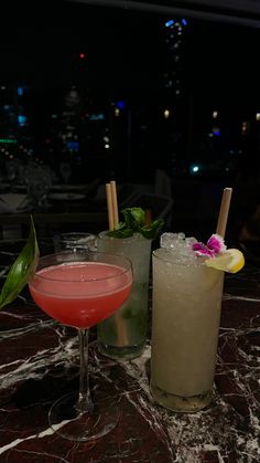 two cocktails sitting on top of a table next to each other with drinks in front of them