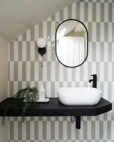 a bathroom sink sitting under a mirror next to a potted plant