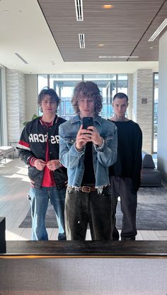 three young men are standing in an airport lobby looking at their cell phones and taking pictures