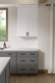 a kitchen with white cabinets and gray counter tops, along with a window over the sink